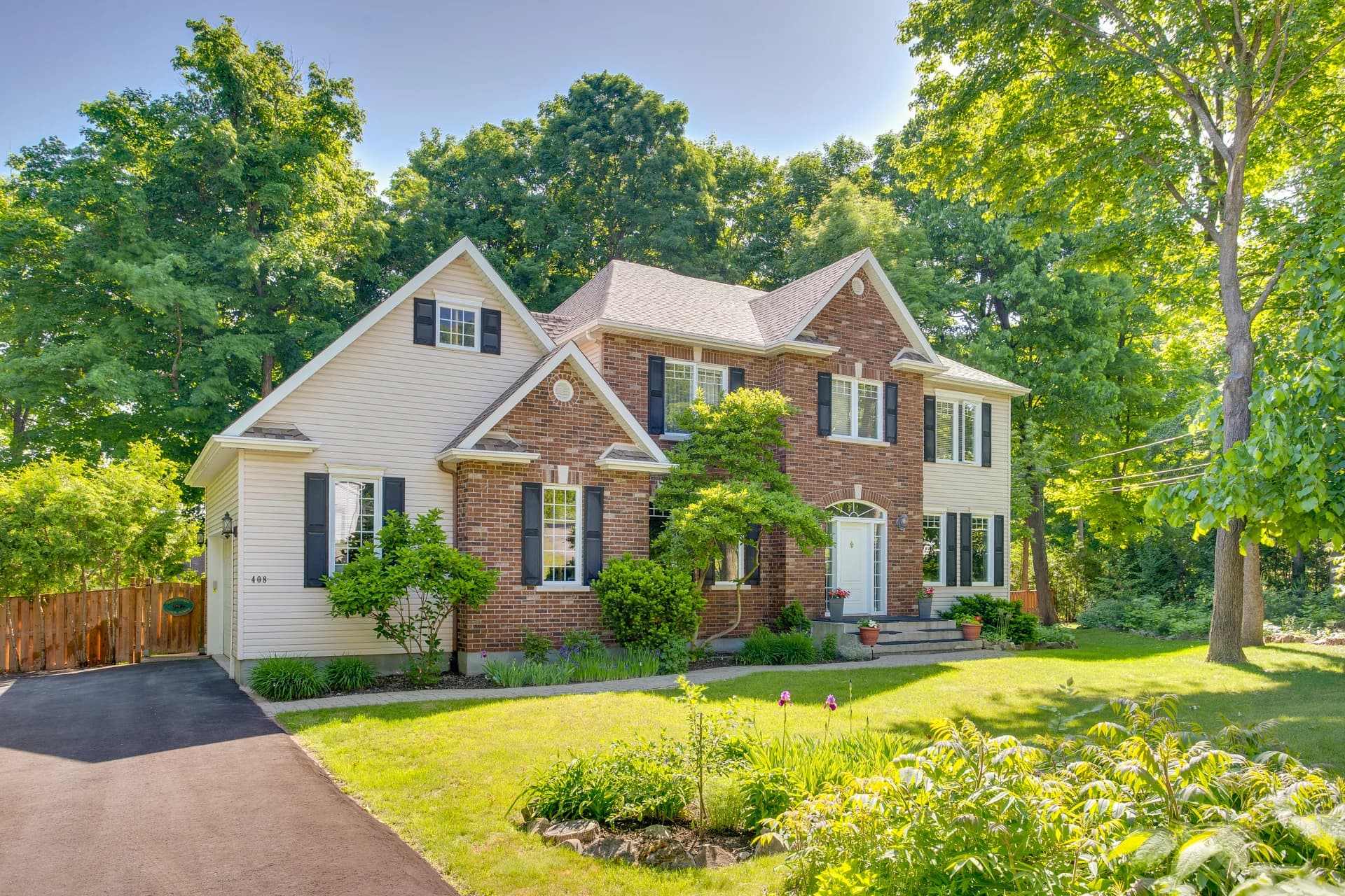Maison en brique et revêtement clair entourée d'arbres en été