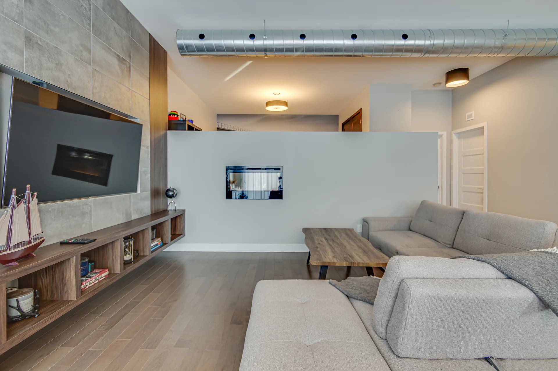 Salon avec téléviseur mural, long meuble en bois et canapé gris
